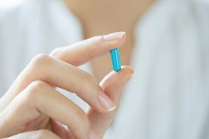 Closeup shot of a woman showing blue capsule pill. Female hand holding a medicine. Shallow depth of field with focus on blue capsule pill.